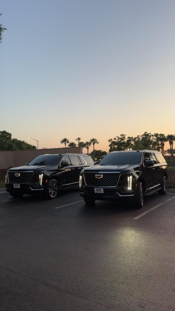 Two black Cadillac Escalade SUVs parked at sunset with palm trees in Orlando